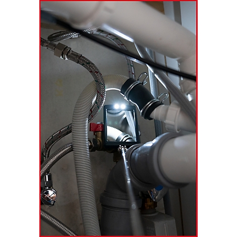 Nahaufnahme von Sanitärinstallationen, beleuchtet mit einem LED-Spiegel. Verschiedene Rohre und Anschlüsse sind zu sehen.